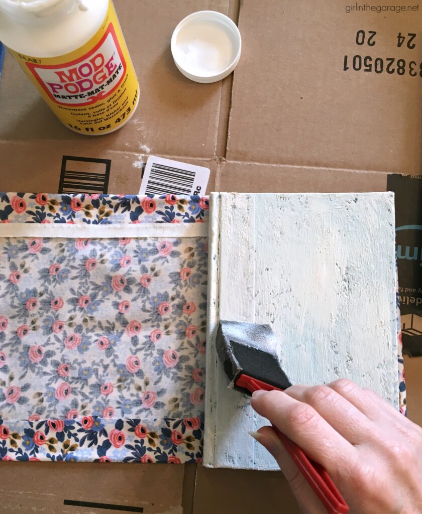 Learn how to decoupage fabric onto books and create gorgeous budget-friendly DIY home decor with this step by step tutorial from Girl in the Garage.